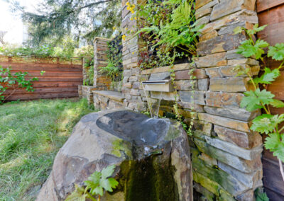 Water flows from the scupper and spills across the basalt boulder into a catch basin below ground, where a pump sends it back to the scupper.